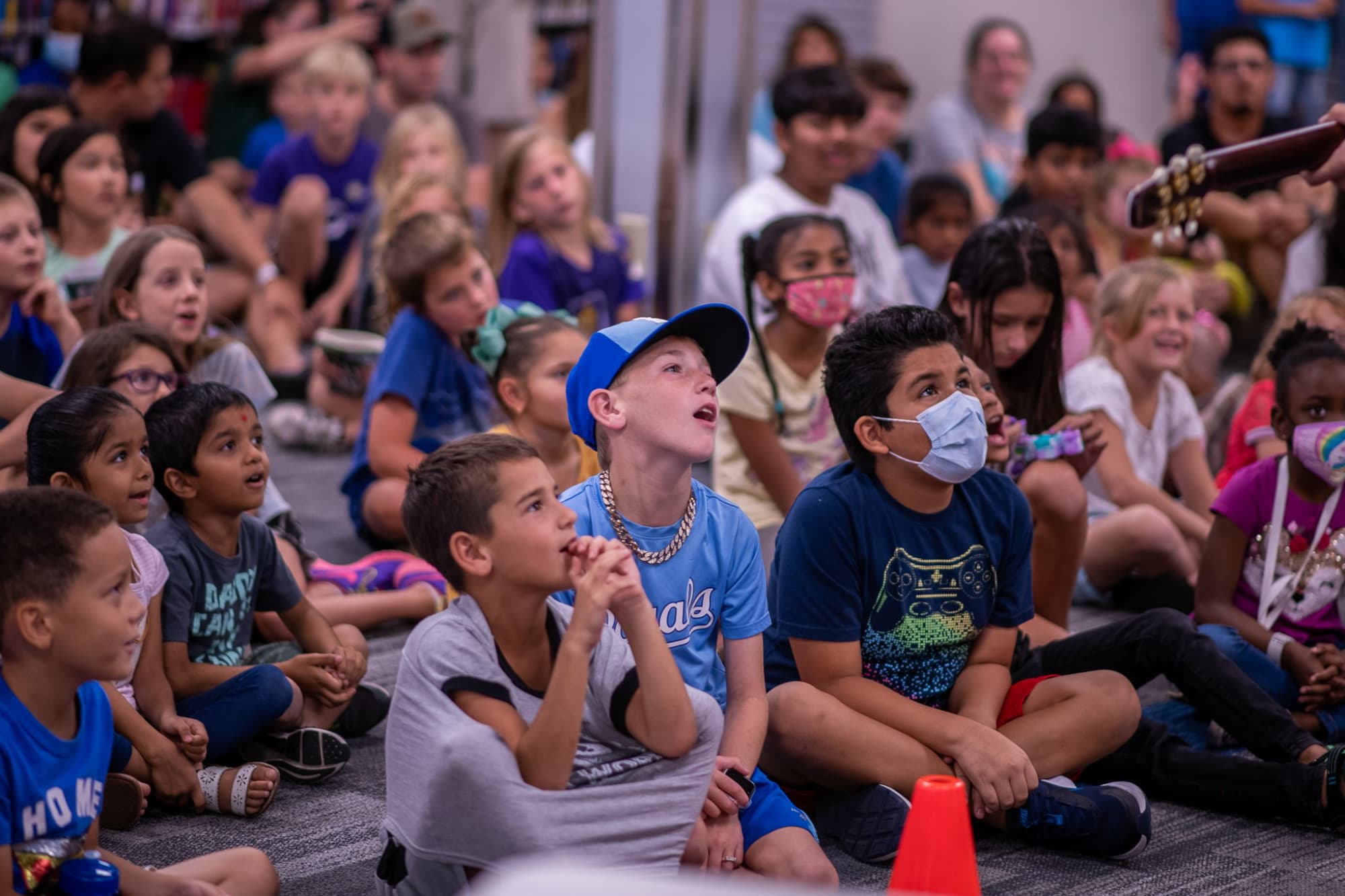 a group of children sitting in a circle with a person wearing a mask