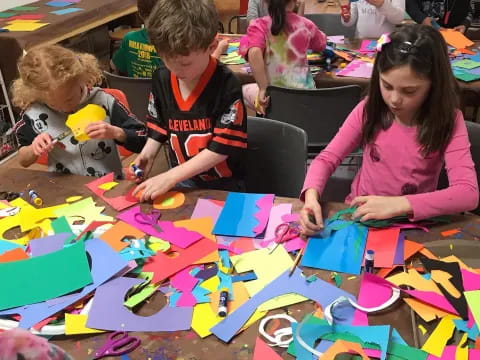 a group of children sitting at a table with colorful pieces of paper