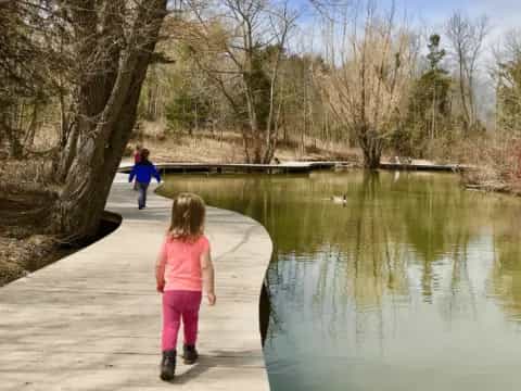 a couple of children walking on a path by a lake with trees