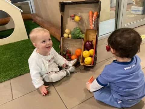 a couple of babies sitting on a tile floor next to a refrigerator