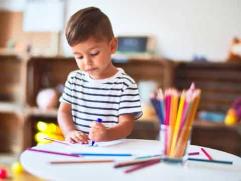 a boy sitting at a table with colored pencils and paper
