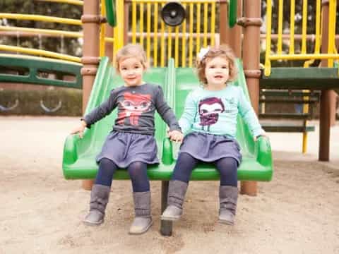two children sitting on a playground swing