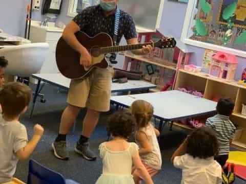a person playing a guitar in a classroom with children